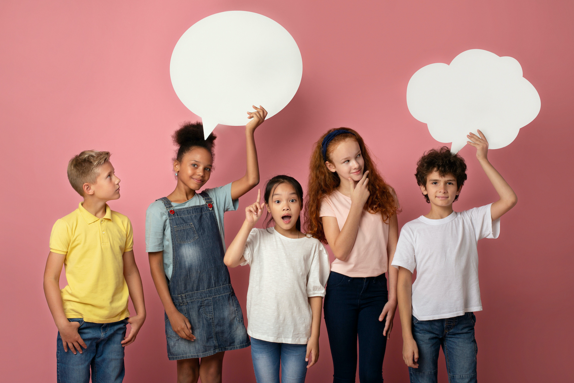 Cute multinational schoolchildren with empty speech bubbles over pink background, space for design Cute multinational schoolchildren with empty speech bubbles on pink background, space for design